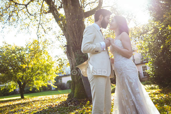 Braut und Bräutigam stehen sich an einem sonnigen Tag im Garten gegenüber — Stockfoto