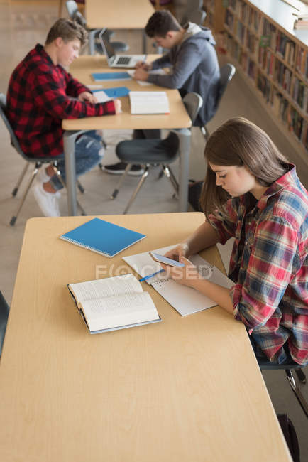 Adolescente estudiante utilizando el teléfono móvil mientras estudia en la biblioteca - foto de stock