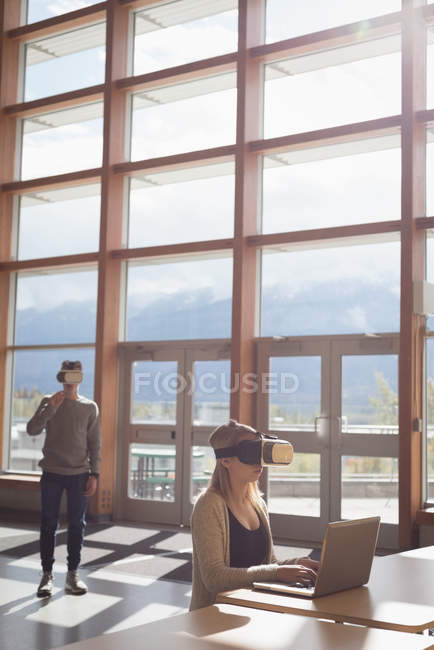Estudantes universitários usando laptop e fone de ouvido de realidade virtual à mesa — Fotografia de Stock