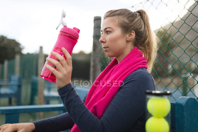 Mujer joven bebiendo agua en pista de tenis - foto de stock