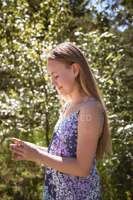 Menina sorrindo olhando para a flor nas mãos no jardim . — Fotografia de Stock