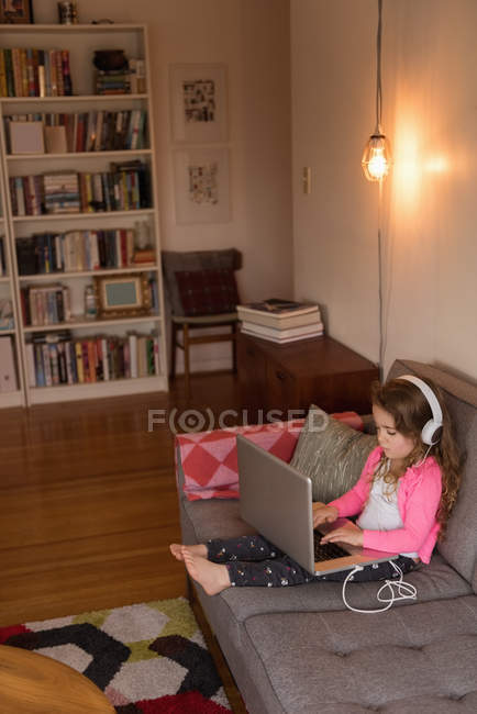 Ragazza che utilizza il computer portatile sul divano in soggiorno a casa — Foto stock