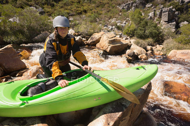 Donna accovacciata con barca kayak su rocce lungo il fiume . — Foto stock