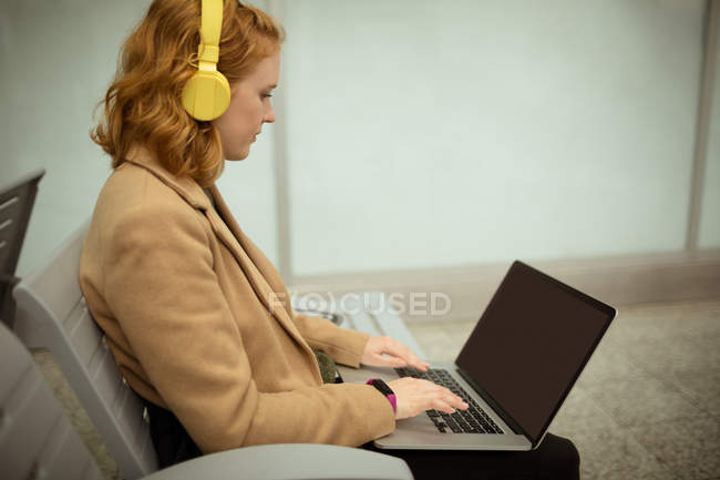 Молодая женщина слушала музыку во время работы на ноутбуке на автобусной остановке — стоковое фото