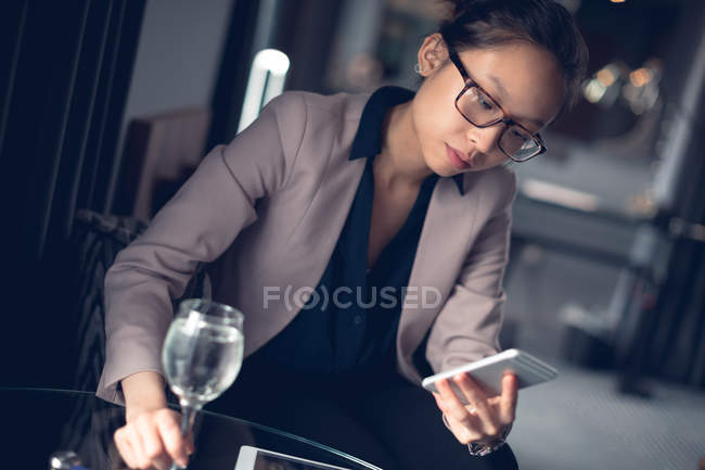 Woman using mobile phone wile having wine in hotel room — Stock Photo
