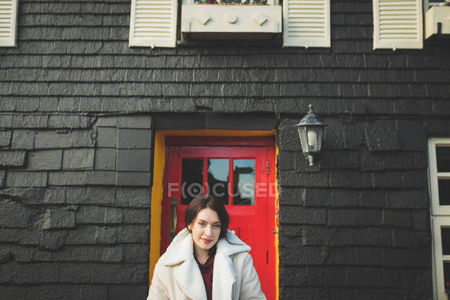 Retrato de mulher em pé na frente da casa com porta vermelha . — Fotografia de Stock