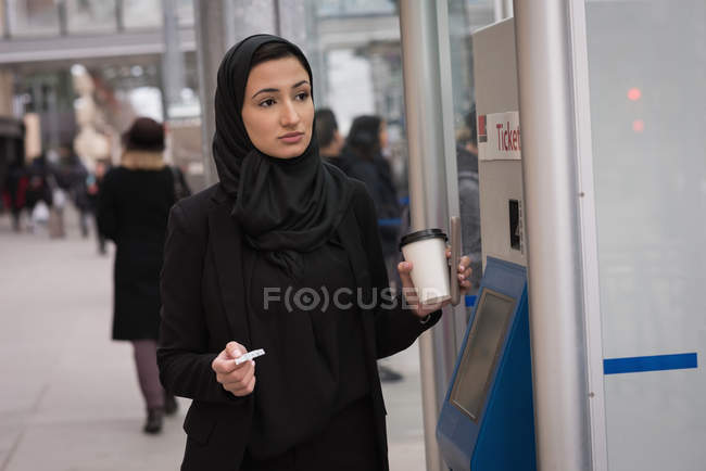 Mujer en hijab sosteniendo taza desechable en la estación de tren - foto de stock