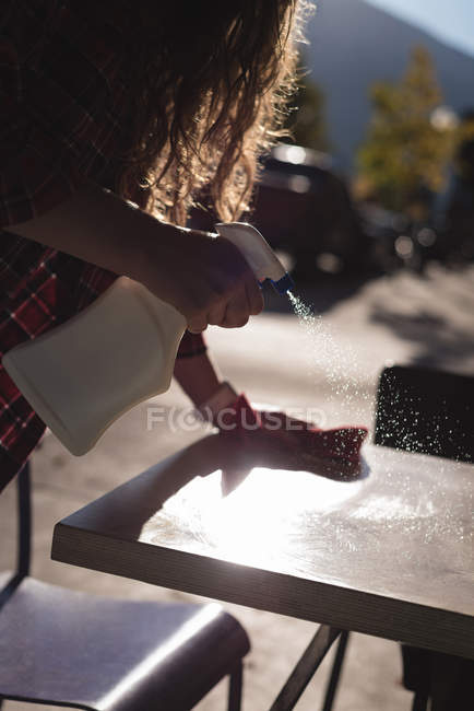 Woman spraying water while cleaning table at outdoor cafe — Stock Photo