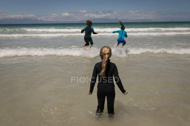 Hermanos en traje de neopreno jugando en olas marinas en un día soleado - foto de stock