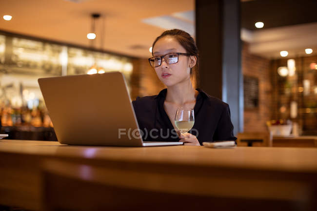 Esecutivo femminile che usa il computer portatile mentre beve vino in hotel — Foto stock