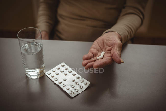 Seção média de uma mulher idosa com comprimidos e um copo de água — Fotografia de Stock