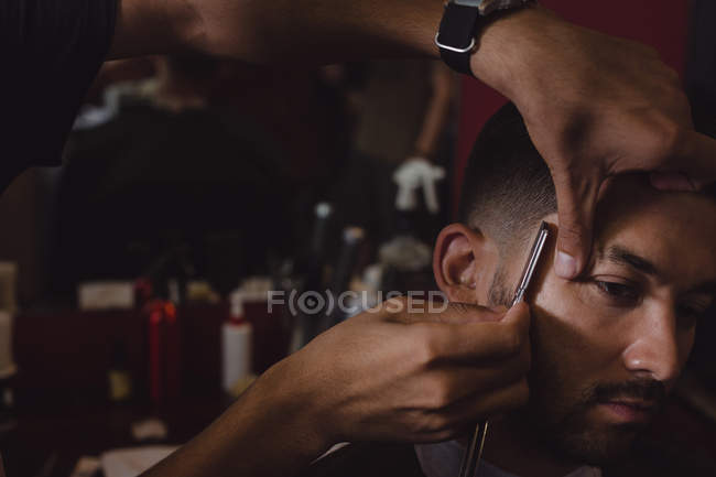 Hombre consiguiendo su pelo recortado con una navaja de afeitar en la barbería - foto de stock