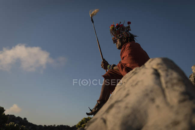 Hombre masai con ropa tradicional sentado en la roca en el campo - foto de stock