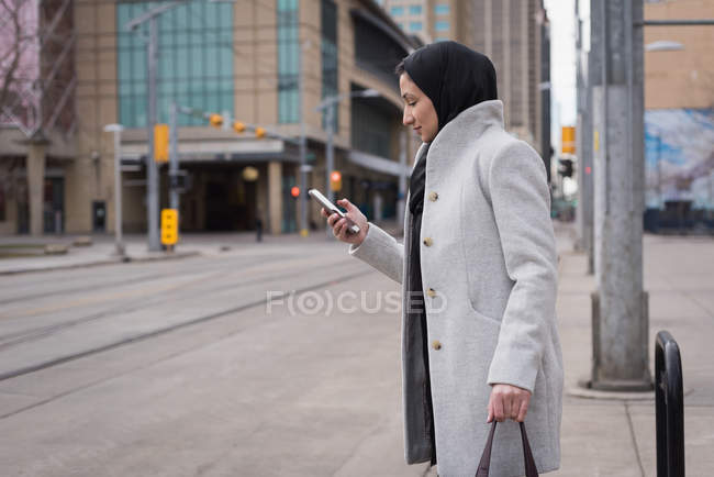 Mujer en hijab usando teléfono móvil en la calle de la ciudad - foto de stock