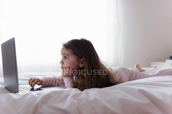 Маленька дівчинка використовує ноутбук у спальні вдома — стокове фото