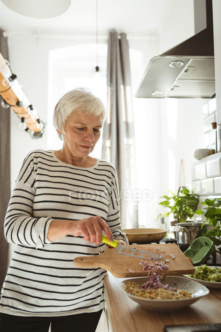 Senior woman adding cut onions to a bowl in the kitchen — Stock Photo
