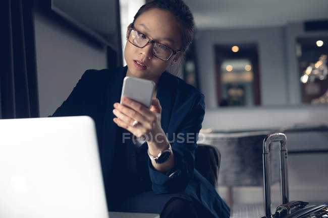 Mujer usando teléfono móvil y portátil en la mesa en la oficina - foto de stock