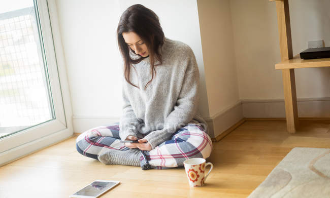 Young woman using mobile phone on floor at home. — Stock Photo