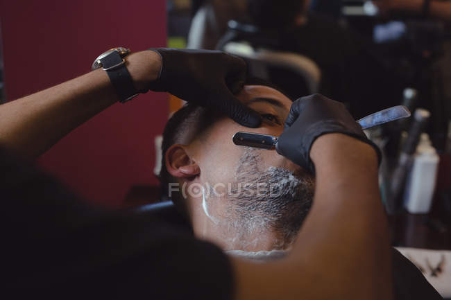 Man getting his beard shaved with straight razor at barbershop — Stock Photo