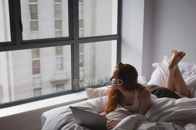 Femme utilisant un ordinateur portable dans la chambre à coucher à la maison — Photo de stock