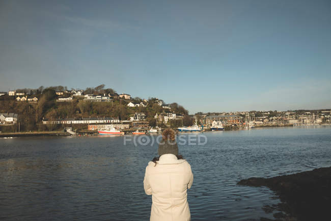 Vue arrière de la femme debout près de la rivière pendant le coucher du soleil . — Photo de stock
