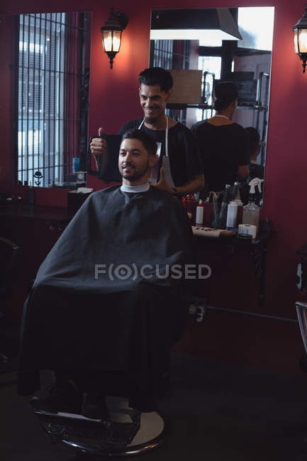 L'uomo che guarda i suoi nuovi capelli tagliati allo specchio dal barbiere — Foto stock