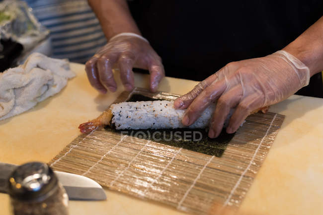 Chef rodando sushi desenrollado sobre tabla de cortar - foto de stock