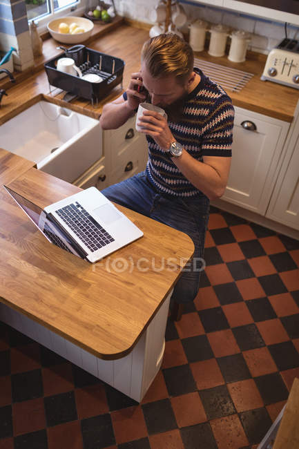Мужчина разговаривает по телефону за чашечкой кофе дома на кухне — стоковое фото