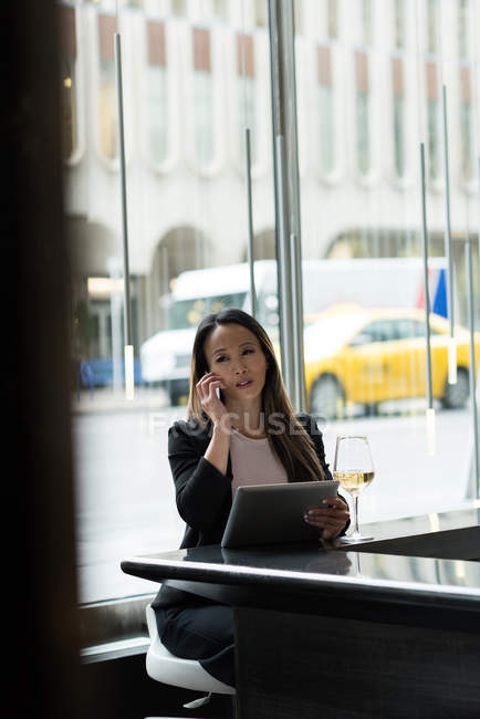 Бізнес-леді розмовляє по телефону, використовуючи свій планшет в кафетерії — стокове фото