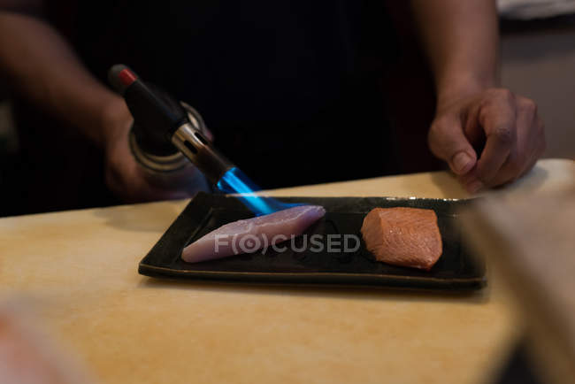 Chef cozinhar fatias de peixe com um maçarico em um restaurante — Fotografia de Stock