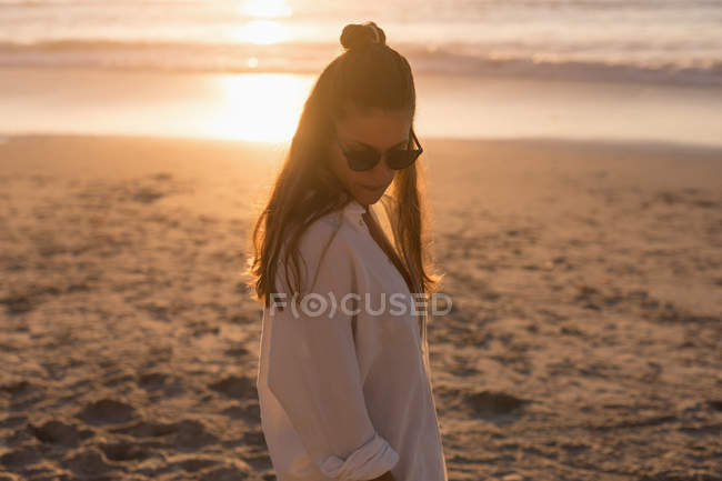 Donna in occhiali da sole in piedi in spiaggia al tramonto
. — Foto stock