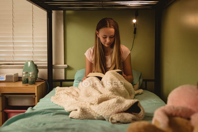 Menina leitura livro enquanto sentado na cama no quarto em casa
. — Fotografia de Stock