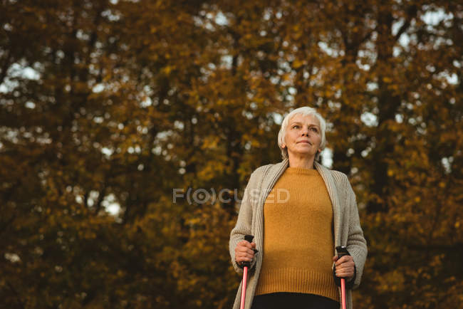 Senior woman walking on a dusty road with walking sticks at the time of dawn — Stock Photo