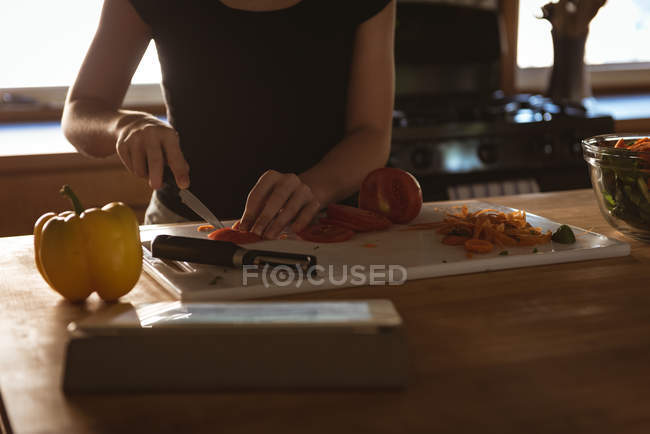 Sección media de chica cortando tomate con cuchillo en cocina . - foto de stock