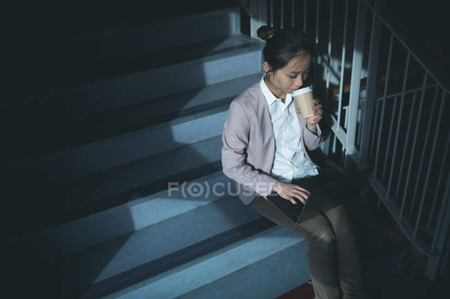Executive utilizzando il computer portatile mentre prende il caffè sulle scale in ufficio — Foto stock