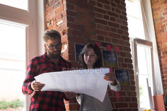 Male and female executives discussing over blueprint in office — Stock Photo