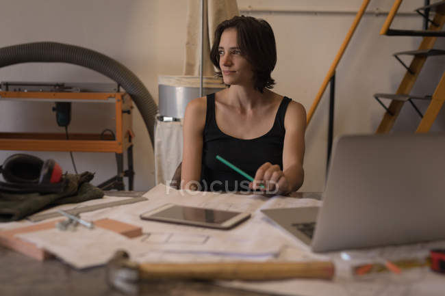 Nachdenkliche Ingenieurin entspannt am Schreibtisch mit Bauplänen in der Werkstatt. — Stockfoto