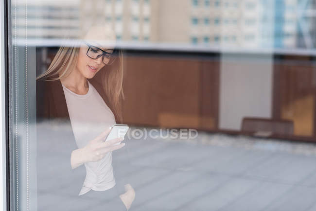 Femme d'affaires asiatique portant des lunettes à l'aide de son téléphone portable dans le hall — Photo de stock