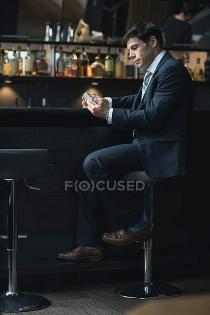 Uomo d'affari che usa il cellulare mentre beve whisky al bancone dell'hotel — Foto stock