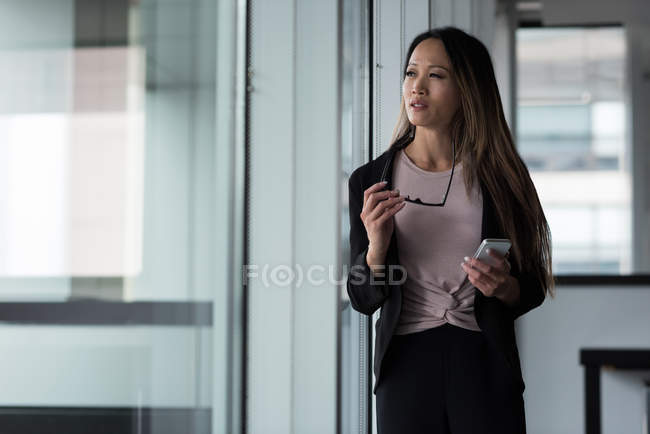 Asiática empresária olhando embora enquanto usa seu telefone celular no lobby — Fotografia de Stock