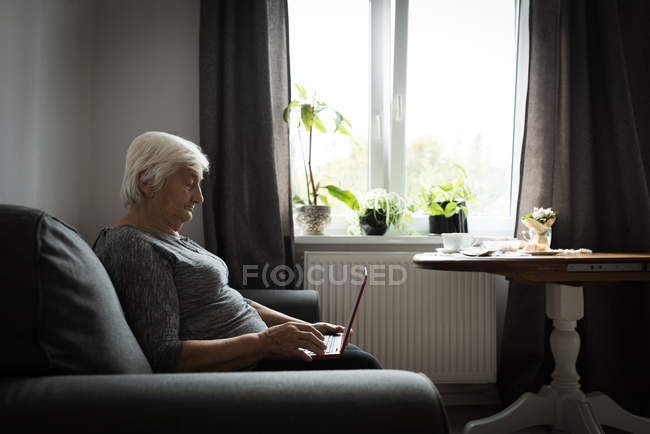Старша жінка використовує ноутбук у вітальні вдома — стокове фото