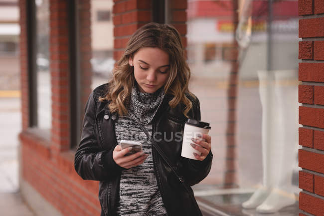 Hermosa chica usando el móvil mientras toma café fuera del centro comercial - foto de stock