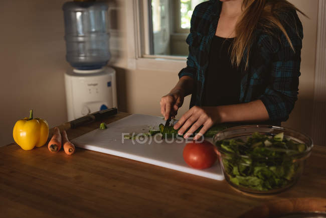 Metà sezione di ragazza in piedi in cucina e il taglio di verdure con coltello a casa . — Foto stock