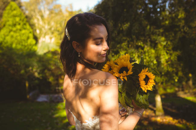 Hermosa novia oliendo un ramo de girasol en el jardín - foto de stock