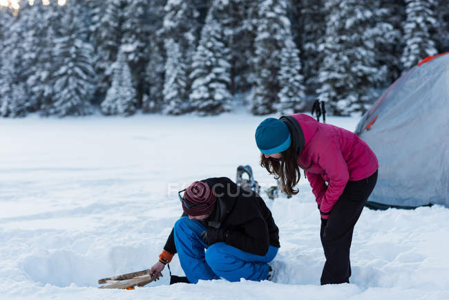 Couple preparing bonfire near tent in snowy woodland during winter. — Stock Photo