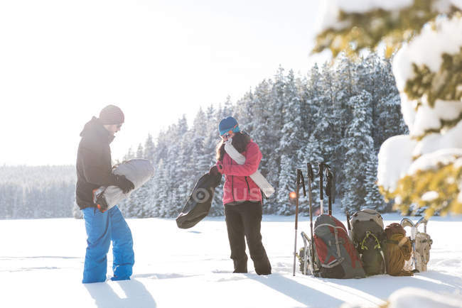 Pareja de pie junto con mochilas y equipo de esquí en el paisaje nevado . - foto de stock