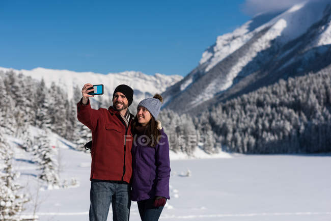 Couple prenant selfie avec téléphone portable dans un paysage de montagne enneigé . — Photo de stock