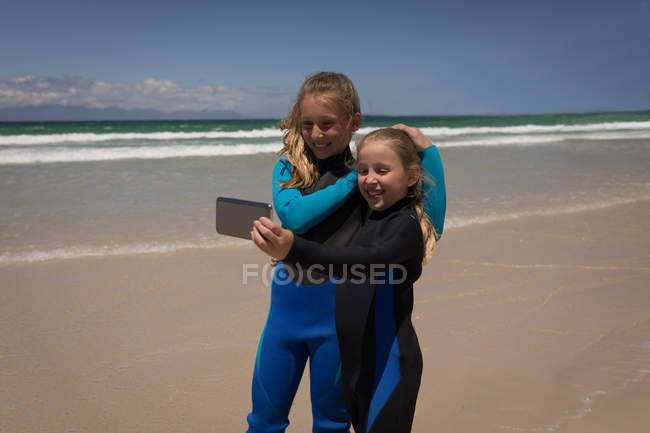 Happy siblings in wetsuit taking selfie with mobile phone on beach — Stock Photo
