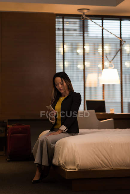Businesswoman sitting on bed using her mobile phone in the hotel — Stock Photo