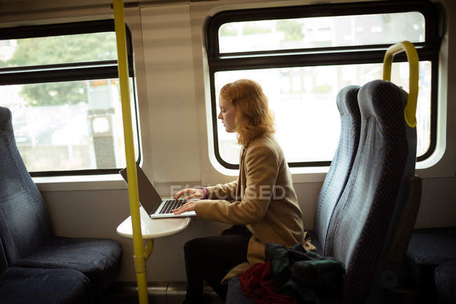 Mujer joven de pelo rojo usando su portátil en tren - foto de stock